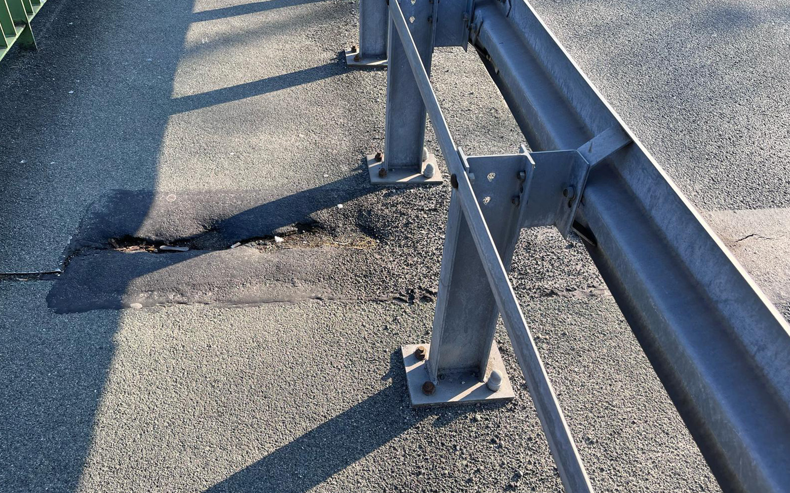 Zdjęcie przedstawia fragment chodnika z metalową barierką. W nawierzchni widoczny spory, niebezpieczny ubytek.