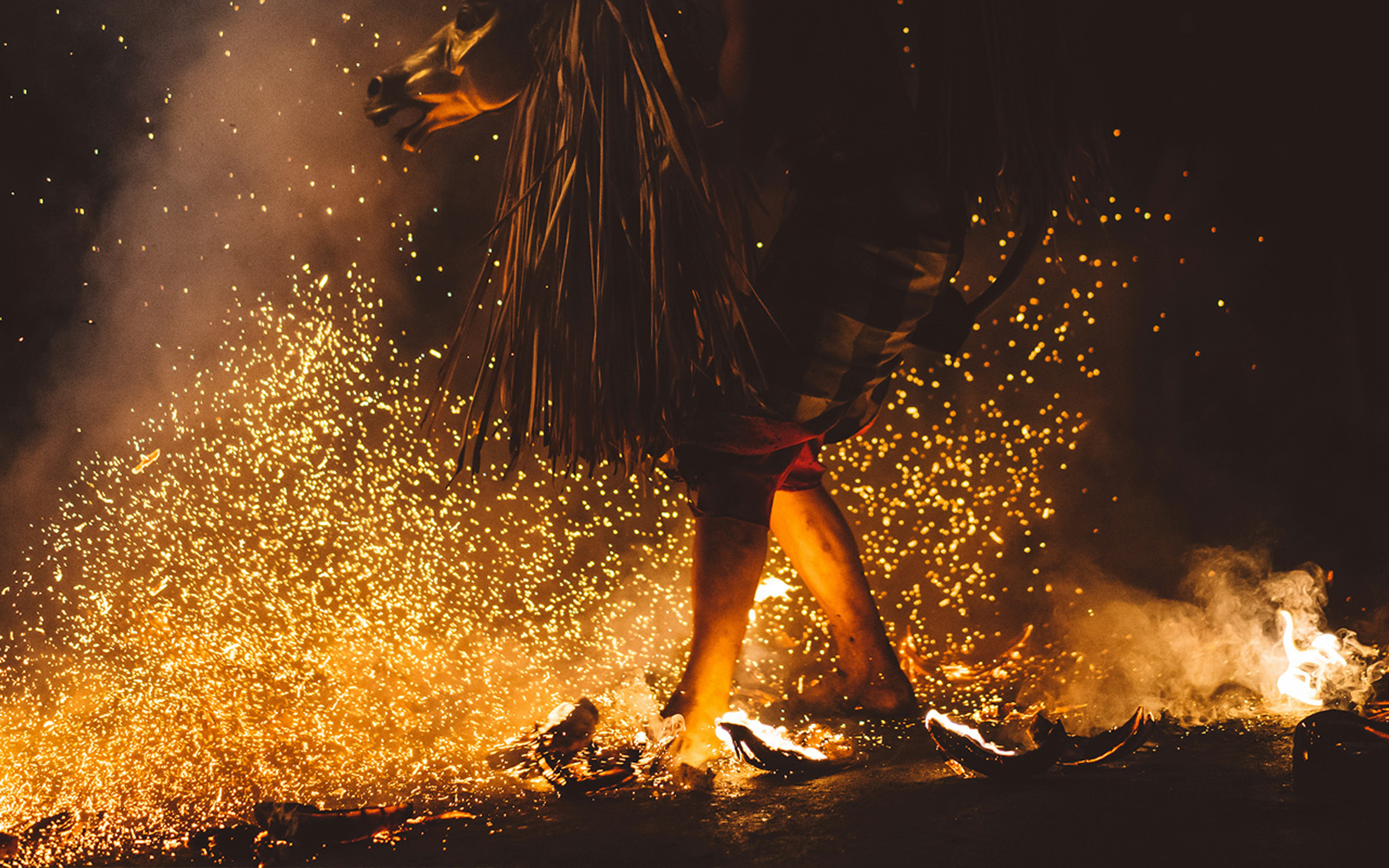 Zdjęcie przedstawia dziwną demoniczną postać kroczącą w ciemności po ogniu i iskrach.