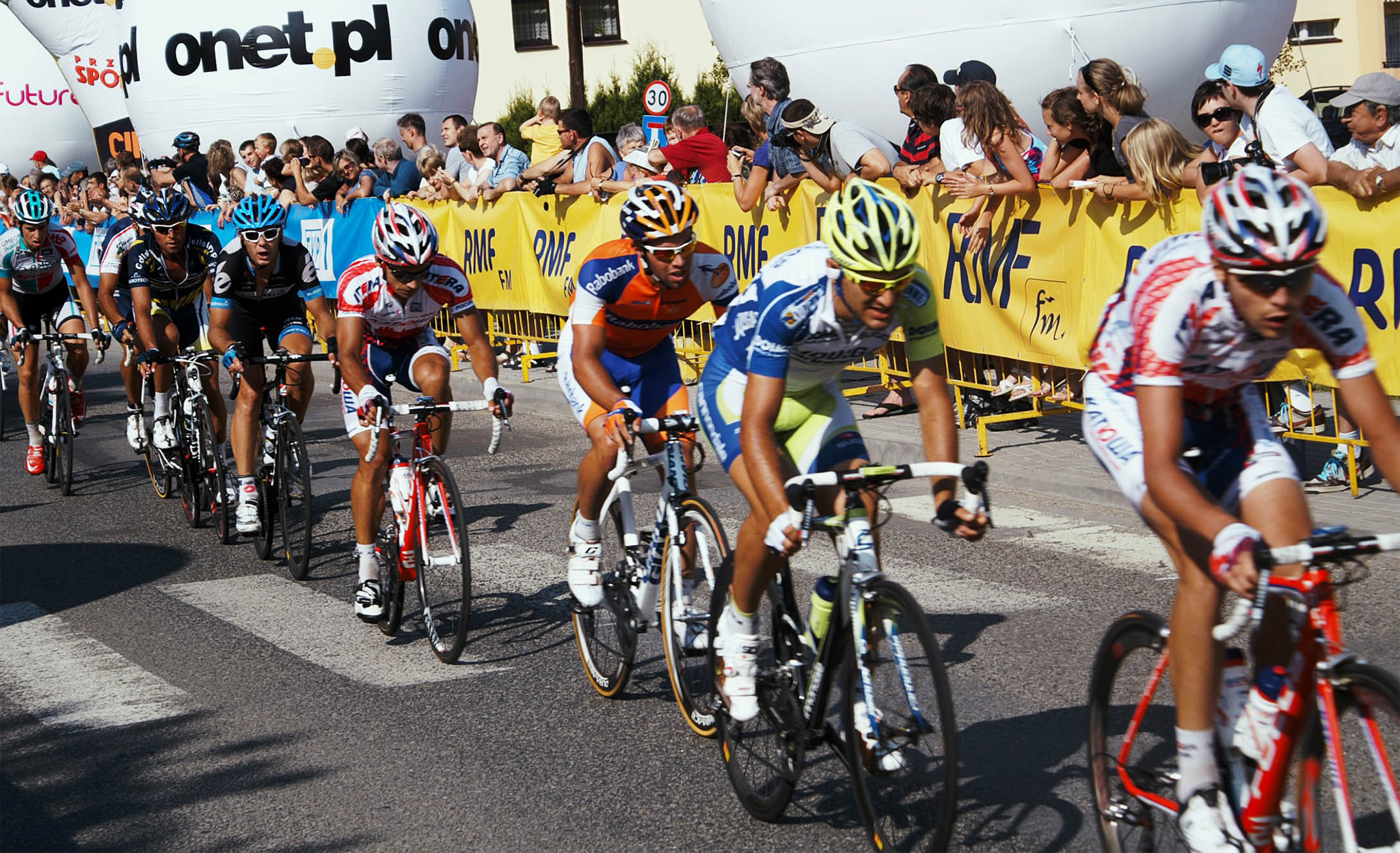 Kolarze przejeżdżający przez Cieszyn. Zdjęcie delikatnie rozmazane przez co oddaje pęd sportowców i ulotność chwili. Na twarzach widać ogromny wysiłek.